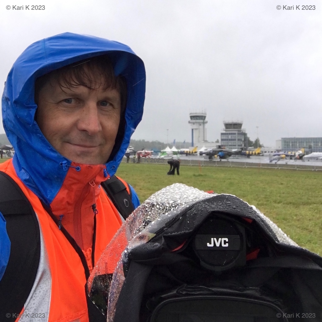 Valokuva henkilöstä videokuvaamassa ulkoilmatapahtumassa sateisena päivänä.